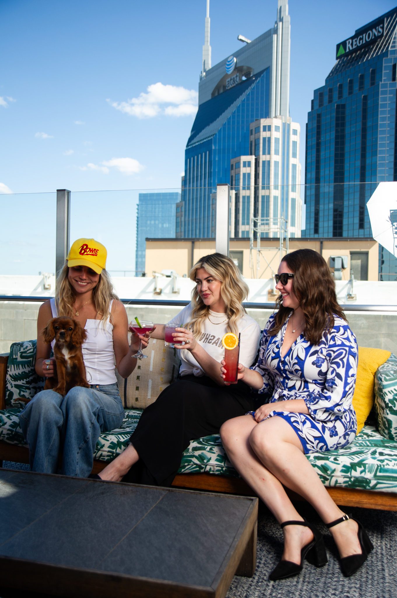 Three women sitting on couch on rooftop with cocktails