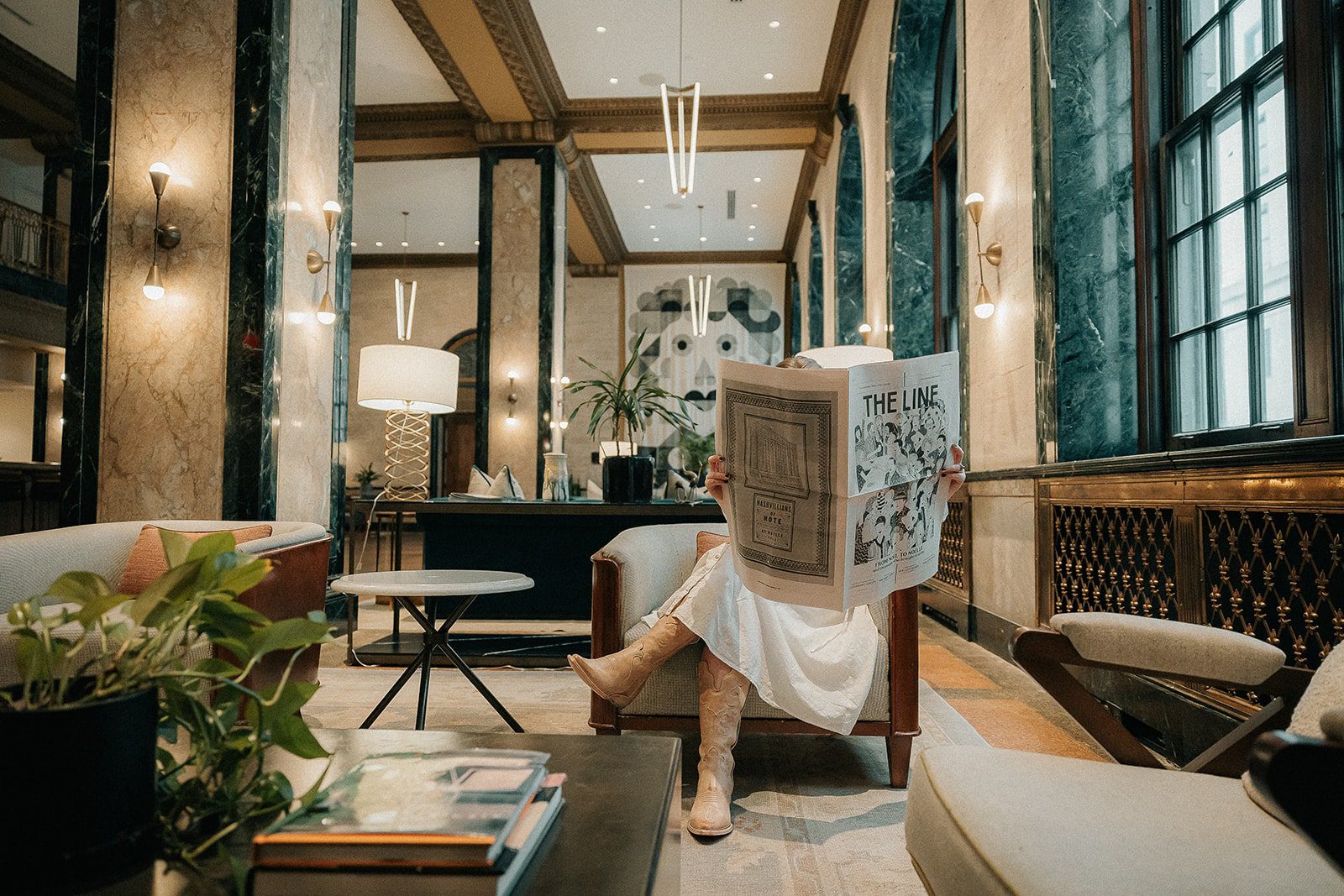 woman sitting on chair holding a newspaper covering her face that says The Line on the masthead